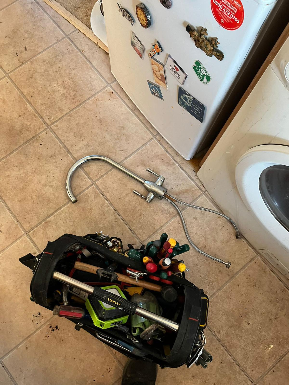 Plumber's tool bag and removed kitchen tap on a tiled floor