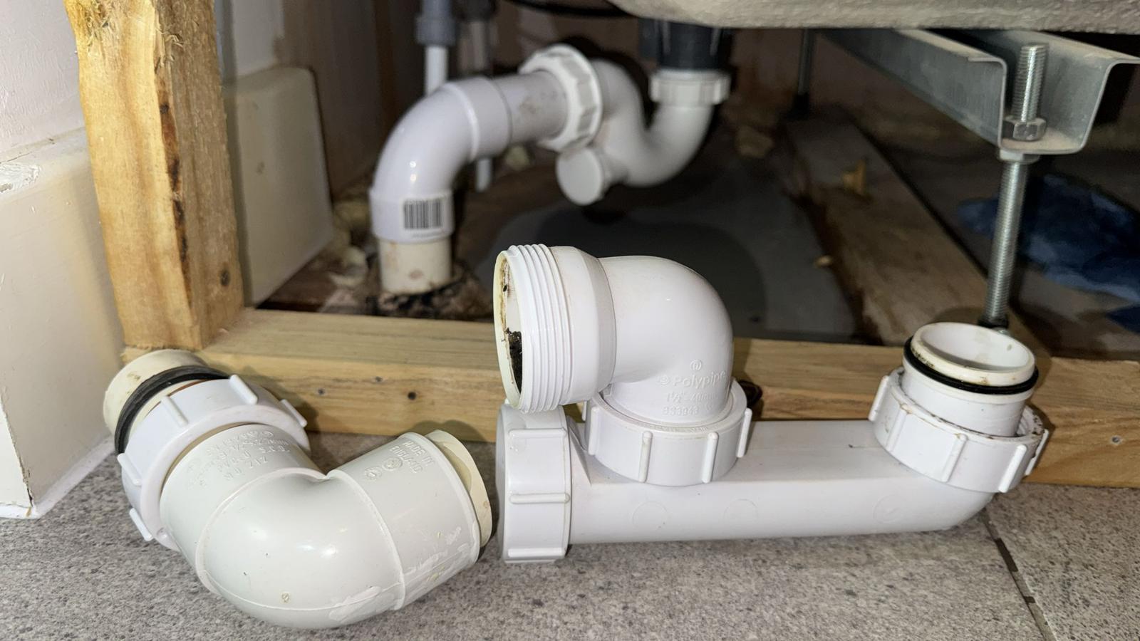 Disassembled plastic waste trap and pipework under a bath